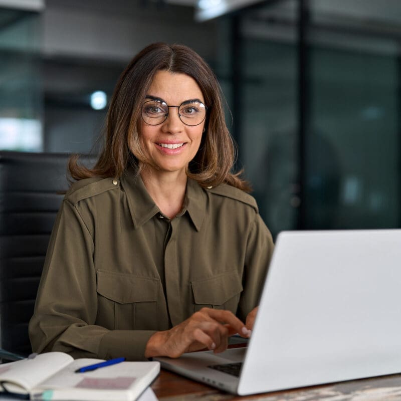 Happy professional business woman of middle age with laptop in office, portrait. Happy mature middle aged professional business woman investor working on laptop computer in office, portrait. Female smiling manager executive or attorney adviser looking at camera at workplace.