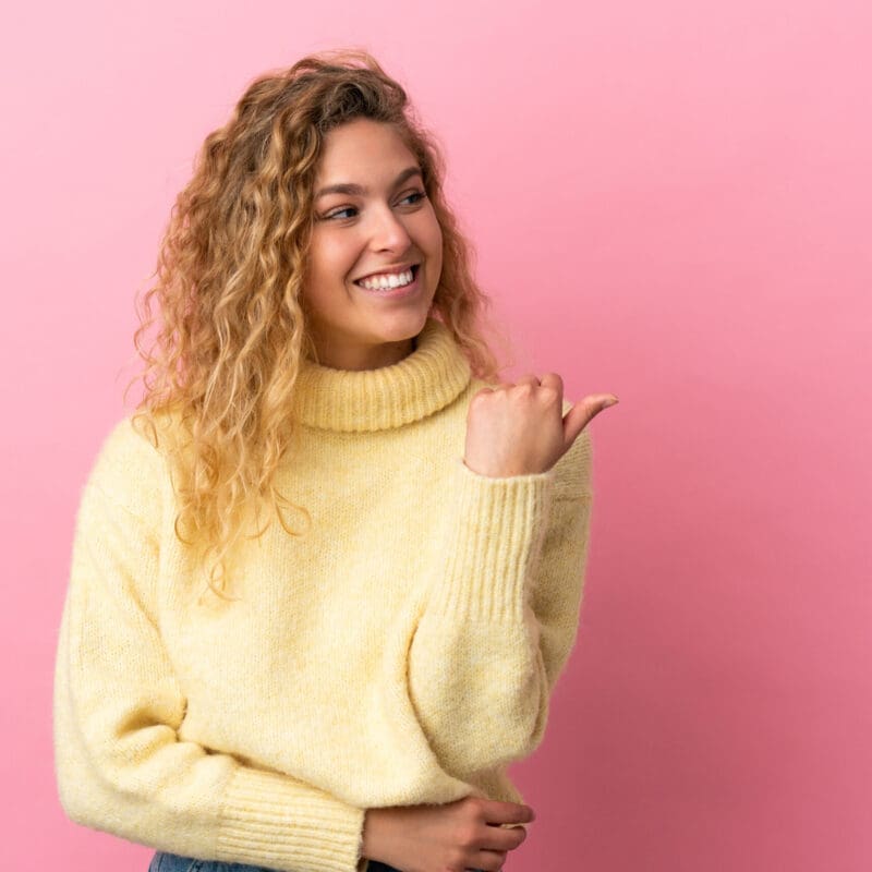 Young Blonde Woman Isolated On Pink Background Pointing To The Side To Present A Product